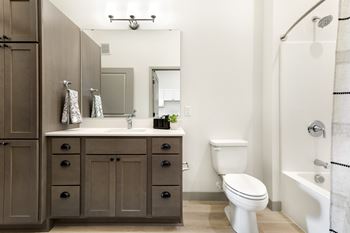 A bathroom with a white toilet, a sink with a mirror, and a shower with a white shower curtain.